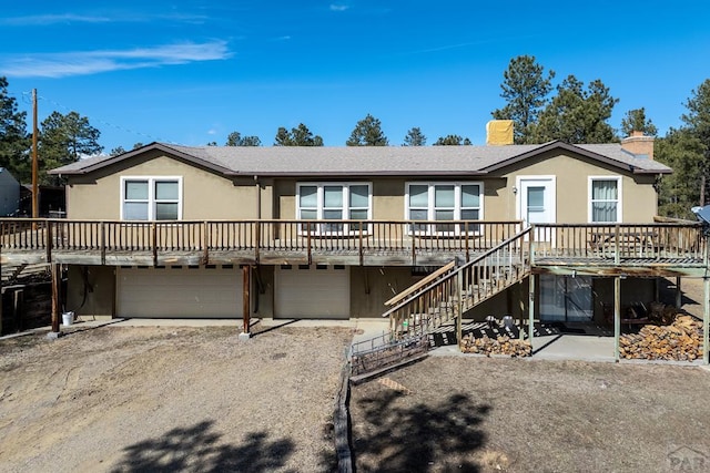 view of front of house featuring driveway, a chimney, an attached garage, stairs, and stucco siding