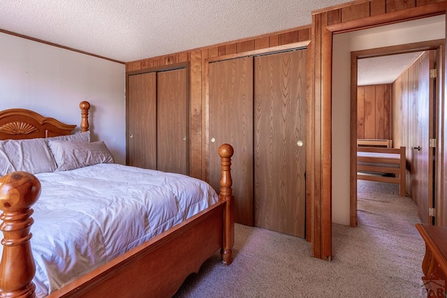 bedroom featuring a textured ceiling, carpet floors, two closets, and wooden walls