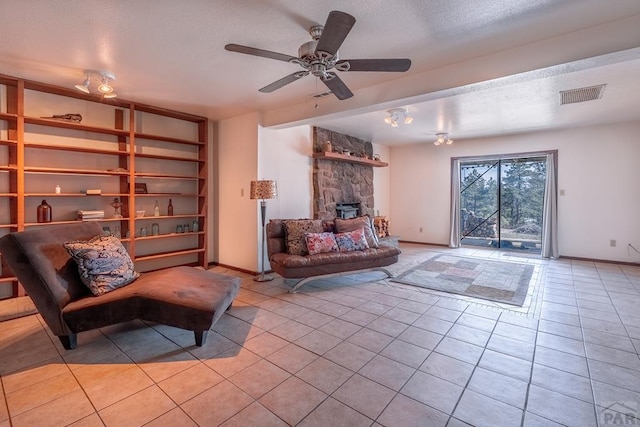 living area with light tile patterned floors, visible vents, a stone fireplace, a textured ceiling, and baseboards