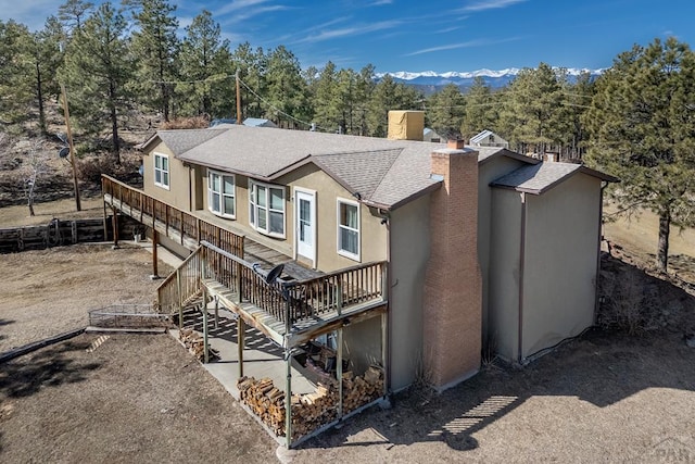 exterior space with a mountain view, stairway, roof with shingles, stucco siding, and a chimney