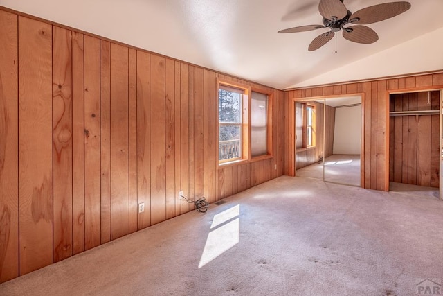 unfurnished bedroom featuring carpet floors, wood walls, vaulted ceiling, and two closets