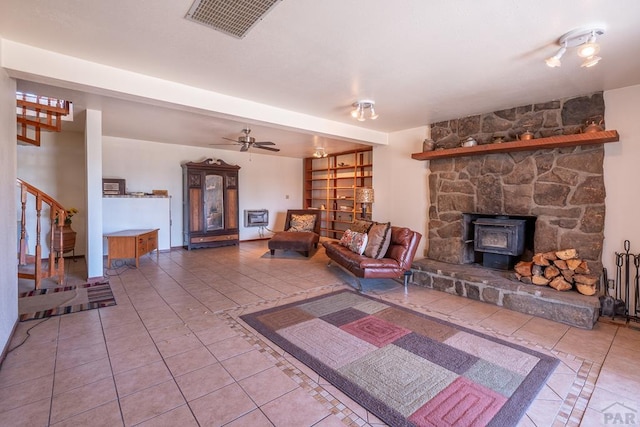 unfurnished living room featuring visible vents, stairway, a ceiling fan, a wood stove, and tile patterned floors