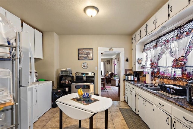 kitchen featuring light tile patterned floors, washer and clothes dryer, stainless steel range with electric stovetop, and white cabinetry