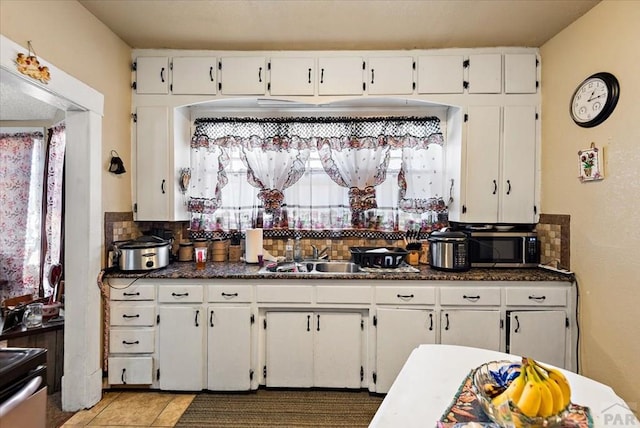 kitchen featuring stainless steel microwave, backsplash, white cabinets, a sink, and tile patterned flooring