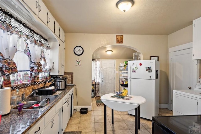 kitchen featuring arched walkways, white cabinets, freestanding refrigerator, a sink, and light tile patterned flooring