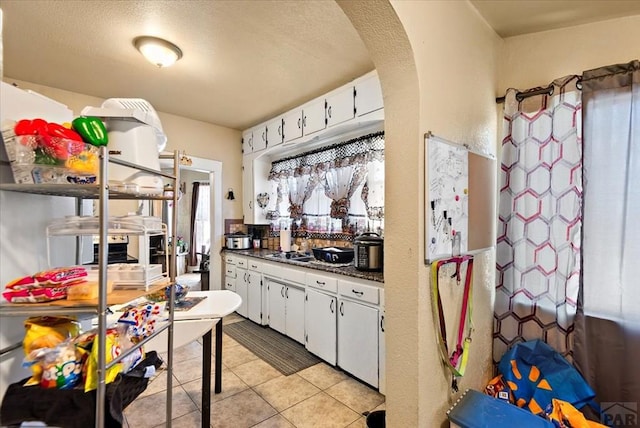 kitchen with dark countertops, light tile patterned floors, white cabinetry, and arched walkways