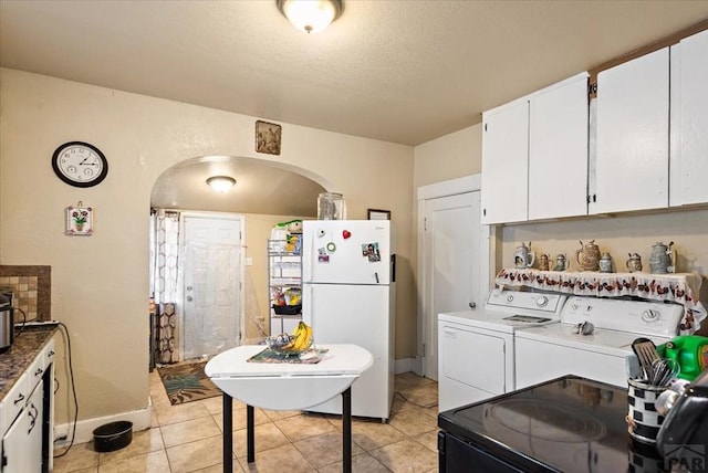 kitchen with arched walkways, washing machine and clothes dryer, freestanding refrigerator, white cabinetry, and light tile patterned flooring