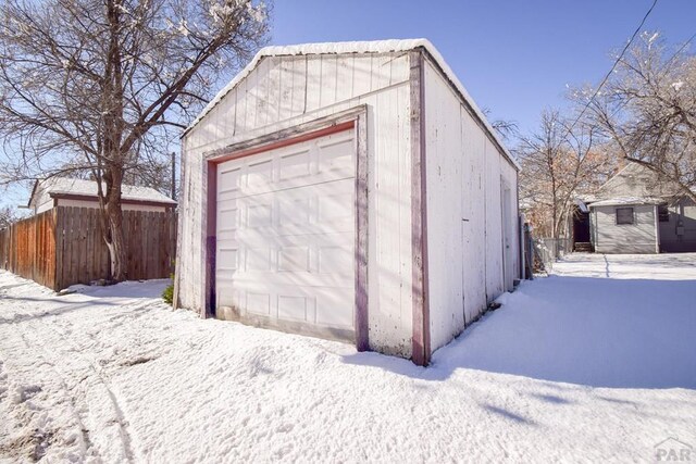 snow covered garage with a detached garage and fence