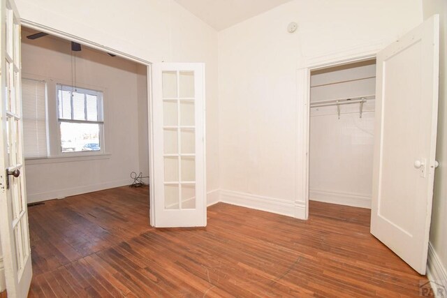 unfurnished bedroom with french doors, dark wood finished floors, a closet, vaulted ceiling, and baseboards