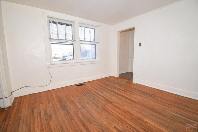 spare room with baseboards, visible vents, and wood finished floors