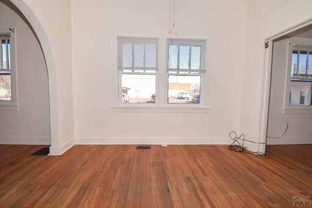 interior space with arched walkways, wood finished floors, visible vents, and baseboards