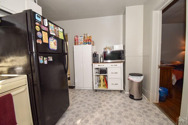 kitchen featuring white cabinets, range, stainless steel microwave, freestanding refrigerator, and light floors