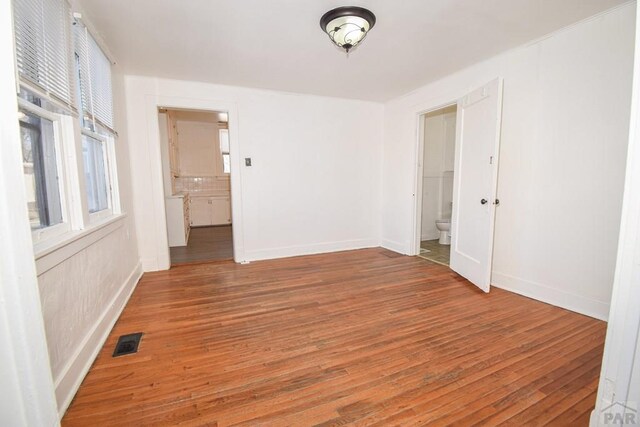 unfurnished room featuring baseboards, visible vents, and wood finished floors