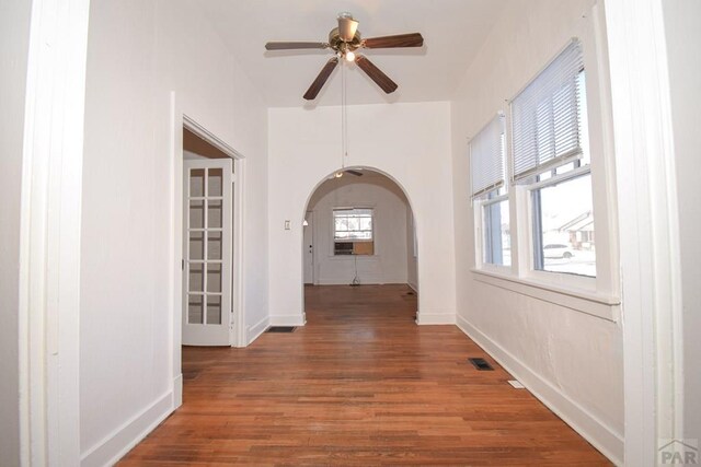 hallway with arched walkways, dark wood-style flooring, visible vents, and baseboards