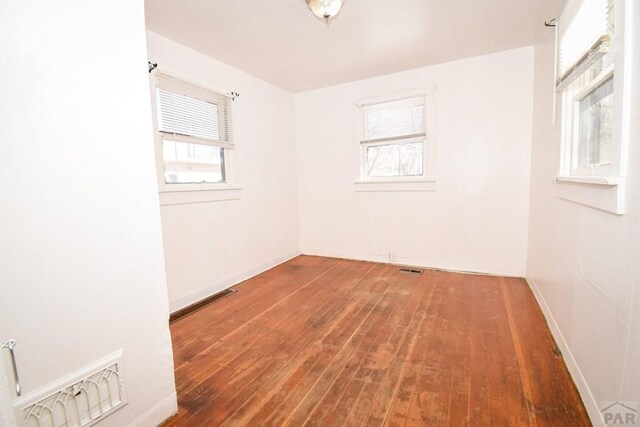 unfurnished room featuring baseboards, visible vents, and wood finished floors