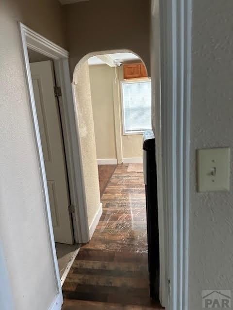 hallway featuring dark wood-type flooring, arched walkways, and baseboards