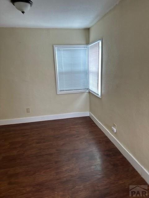 unfurnished room with dark wood-type flooring and baseboards