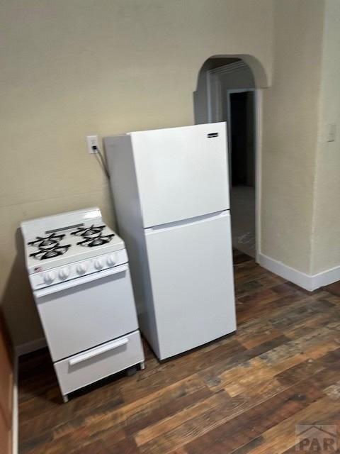 kitchen featuring dark wood-type flooring, white appliances, and baseboards