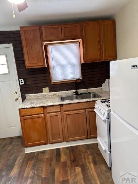 kitchen with brown cabinets, white appliances, dark wood-style flooring, and a sink