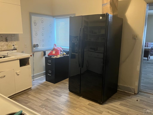 kitchen featuring tasteful backsplash, light countertops, black fridge with ice dispenser, light wood-style floors, and white cabinets