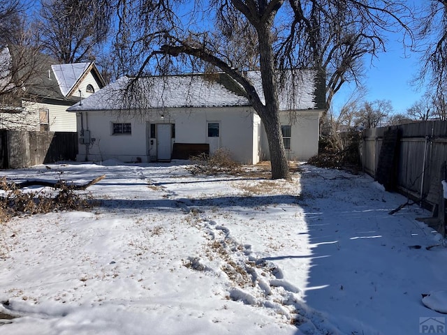 snow covered house with fence and stucco siding