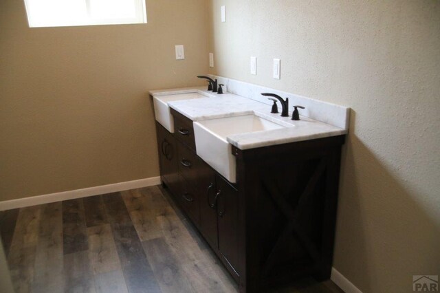 bathroom with double vanity, a sink, baseboards, and wood finished floors