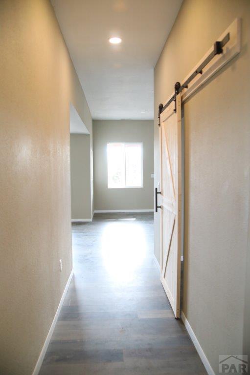 corridor featuring a barn door, baseboards, and dark wood-type flooring