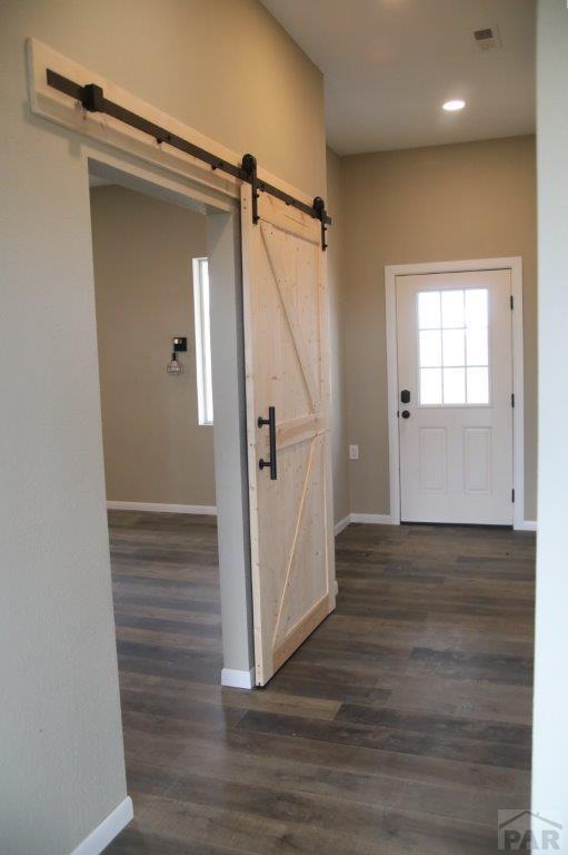 foyer with baseboards, a barn door, visible vents, and dark wood-style flooring