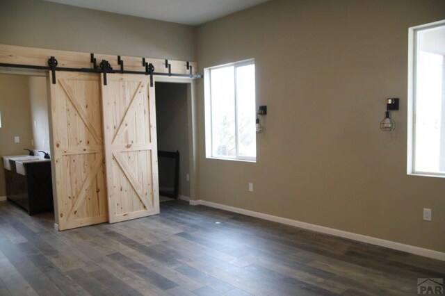 unfurnished bedroom with a barn door, multiple windows, baseboards, and dark wood-type flooring