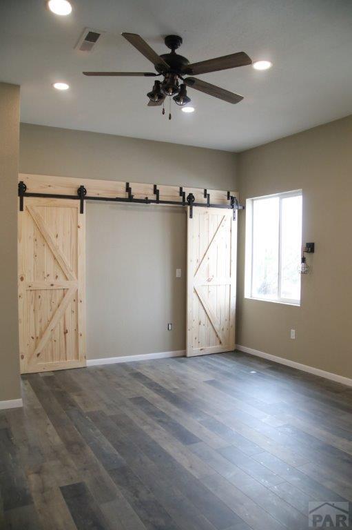 unfurnished room with a barn door, baseboards, dark wood-type flooring, and recessed lighting