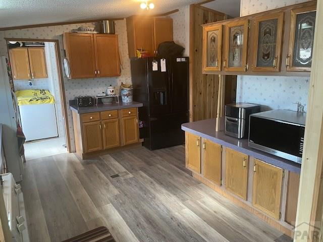 8417 3r Rd, Beulah, CO 80123 - kitchen with wallpapered walls, stainless steel microwave, black fridge with ice dispenser, brown cabinetry, and a textured ceiling
