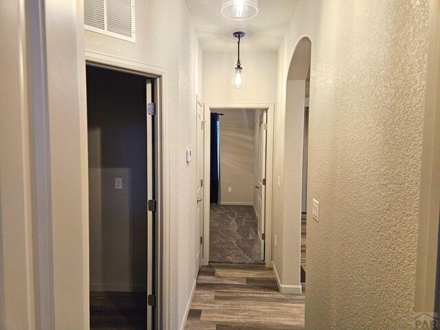 hall with dark wood-style flooring, visible vents, a textured wall, and baseboards