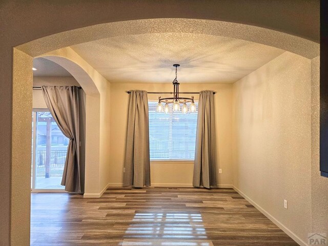 unfurnished dining area with arched walkways, a textured ceiling, and wood finished floors