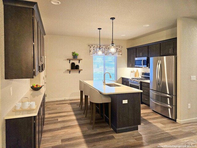 kitchen featuring a kitchen island with sink, stainless steel appliances, a sink, light countertops, and decorative light fixtures