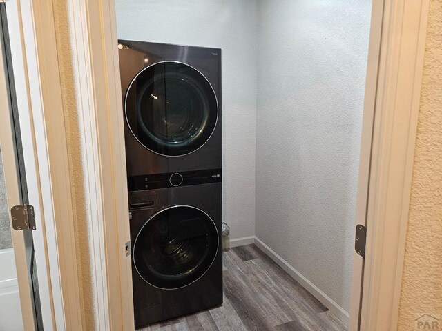 laundry area with stacked washer / drying machine, a textured wall, wood finished floors, laundry area, and baseboards