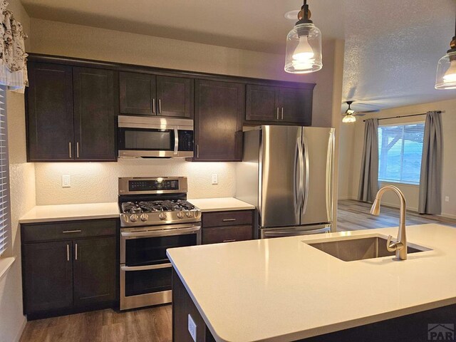 kitchen with light countertops, hanging light fixtures, appliances with stainless steel finishes, a kitchen island with sink, and a sink