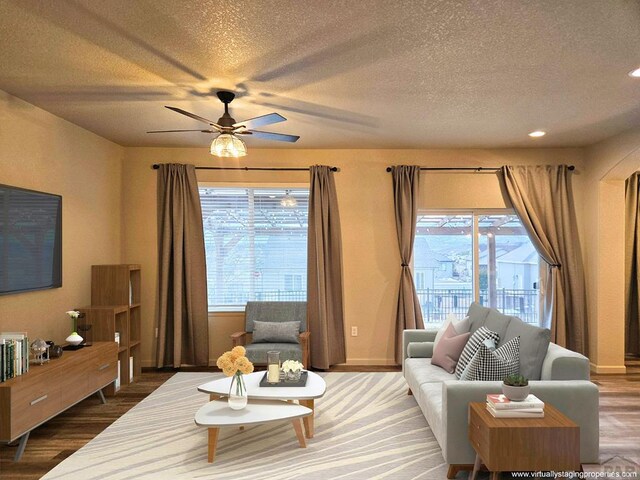 living area with a ceiling fan, a textured ceiling, baseboards, and wood finished floors