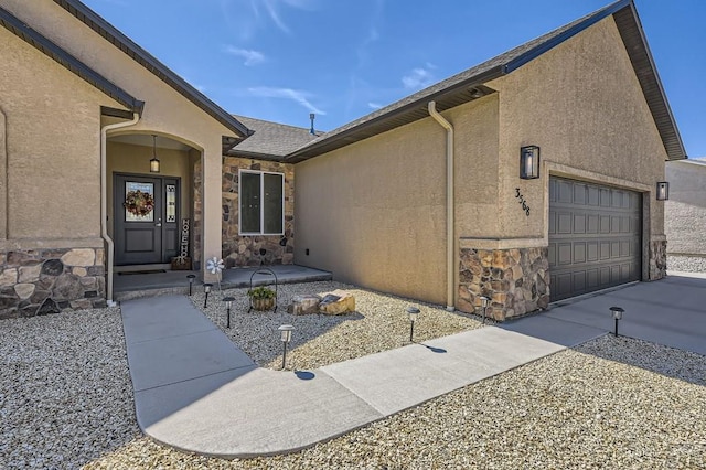 entrance to property with stone siding, an attached garage, and stucco siding