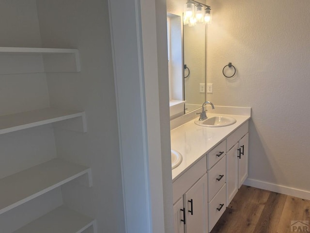 bathroom with double vanity, baseboards, a sink, and wood finished floors