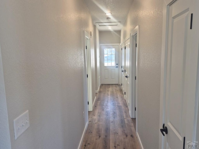 hall with a textured wall, a textured ceiling, baseboards, and wood finished floors