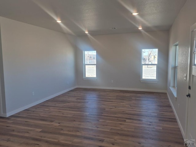 spare room with a textured ceiling, dark wood-style flooring, plenty of natural light, and baseboards