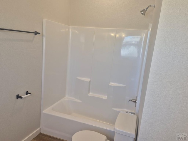 bathroom with a textured wall, shower / bathing tub combination, toilet, and wood finished floors