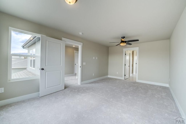 interior space featuring baseboards, a ceiling fan, and light colored carpet