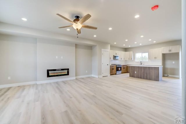unfurnished living room with recessed lighting, a ceiling fan, baseboards, light wood-style floors, and a glass covered fireplace