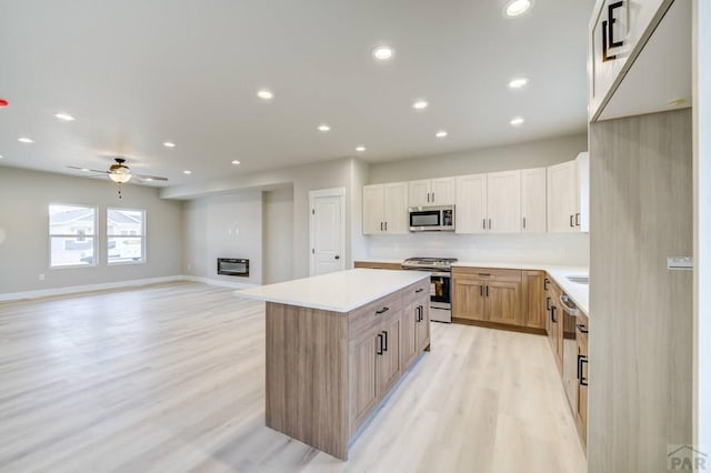 kitchen with stainless steel appliances, open floor plan, light countertops, a center island, and light brown cabinetry