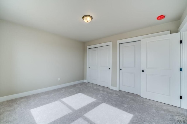 unfurnished bedroom featuring multiple closets, light carpet, and baseboards
