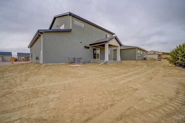 back of house with stucco siding and central air condition unit
