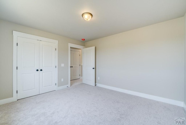 unfurnished bedroom with a closet, light carpet, and baseboards
