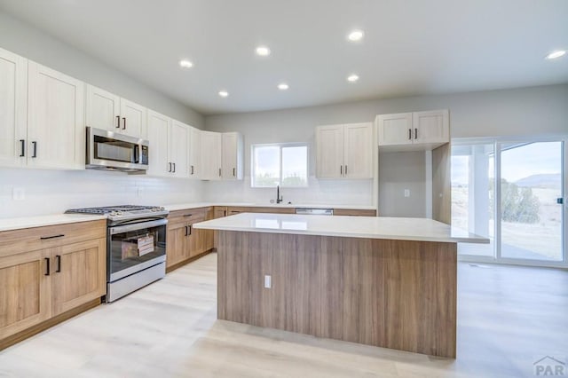 kitchen with light countertops, appliances with stainless steel finishes, white cabinetry, a kitchen island, and a sink