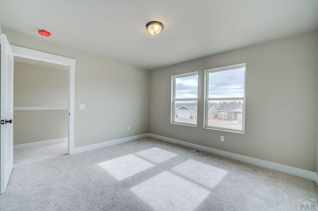 spare room featuring light carpet and baseboards